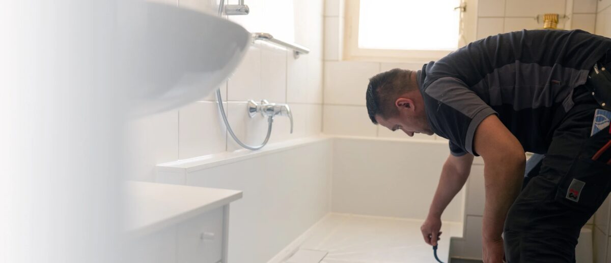 Ein Handwerker streicht die Innenwände einer Dusche